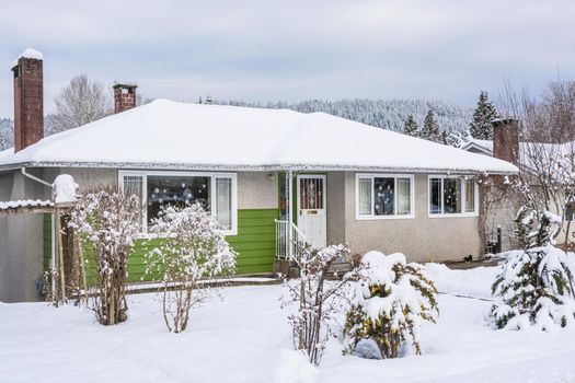 Family house with front yard in snow. Colorful residential house on winter cloudy day