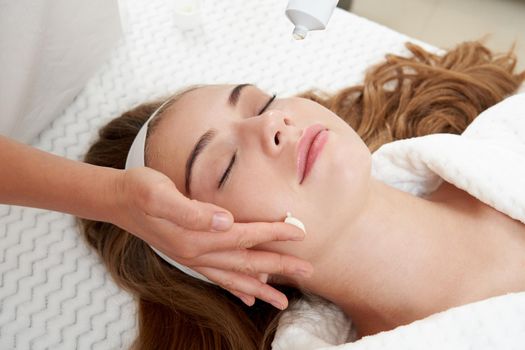 Cosmetologist applying cream on patient face, portrait closeup view. Woman in beauty clinic with doctor beautician