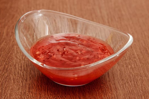 glass saucer with hot chili sauce on wooden table. indoor closeup