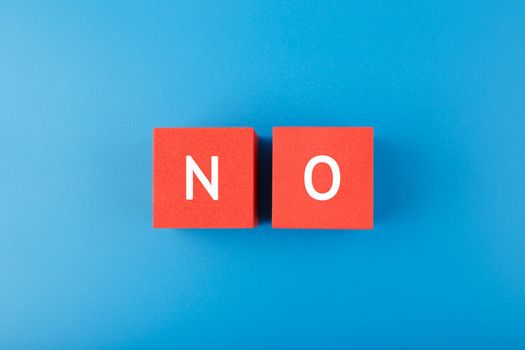 Flat lay with single word no on red cubes against blue background. Say no to violence, toxic people, discrimination, agism and other negative factors