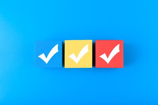 Three checkmarks on multicolored cubes in a row on blue background with copy space. Concept of questionary, checklist, to do list, planning, business or verification. Modern minimal composition