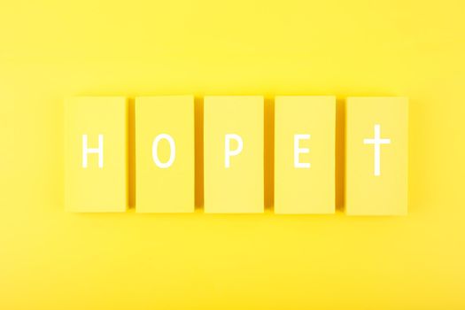 Modern religious minimal concept of hope with christian cross on bright yellow background. Biblical creative composition with single word hope and cross