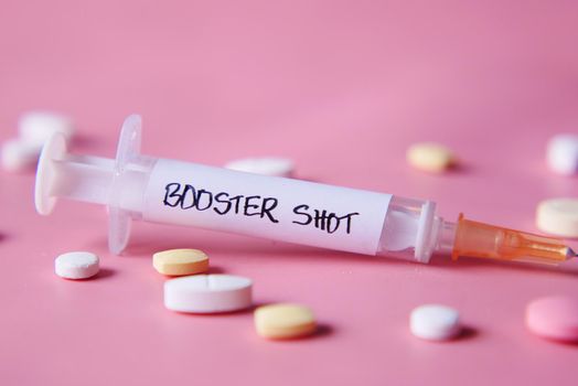 booster shot test on syringe and pills on pink background, close up,