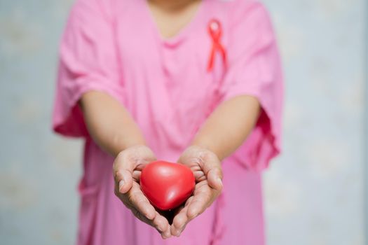 Asian lady woman patient holding red heart in hand at hospital, symbol of World Breast Cancer Day.