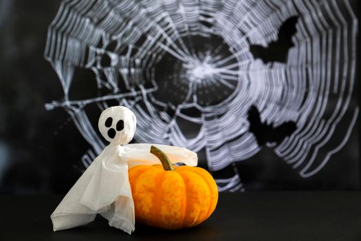 White ghost sits on branch against background of cobwebs and bats. Concept of halloween .