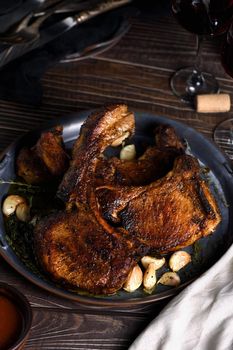 Juicy, slice of fried pork chop on a bone in oil with garlic and herbs in a pan. Close-up.