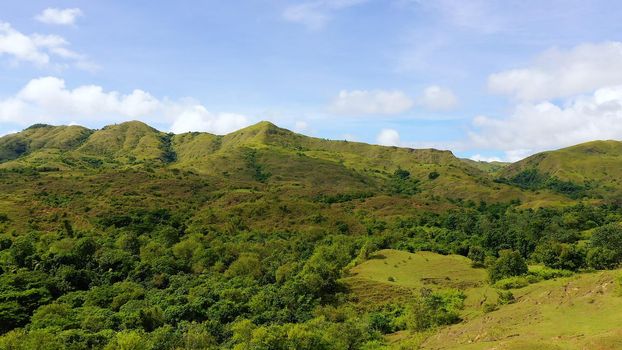 Hills with green grass and blue sky with white puffy clouds. Beautiful landscape on the island of Luzon, aerial view.