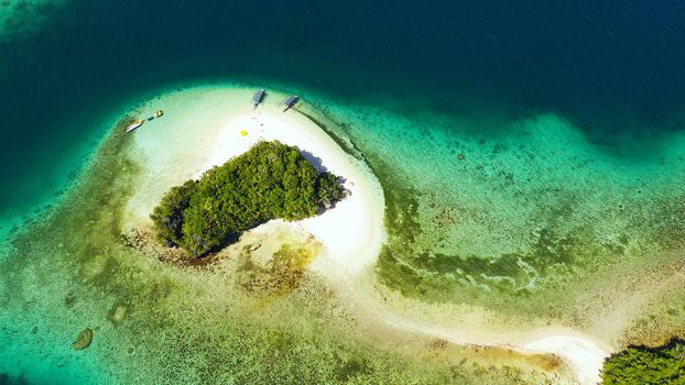 Small Island with beautiful beach, palm trees by turquoise water view from above. Britania Islands, Surigao del Sur, Philippines.