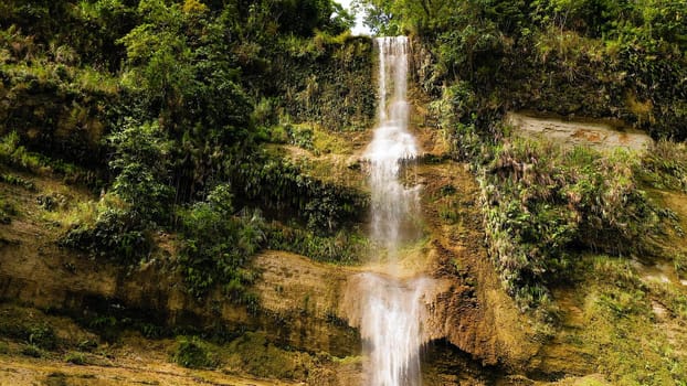Aerial top view of jungle Waterfall in a tropical forest surrounded by green vegetation. Can-umantad Falls in mountain jungle. Bohol, Philippines.