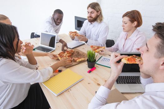 Happy diverse colleagues have fun at lunch break in office, smiling multiracial employees laugh and talk eating pizza