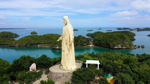 Sculpture of Jesus Christ on an island located in a Hundred Islands National Park, Pangasinan, Philippines. Aerial drone: cluster of Islands with beaches and lagoons, famous tourist attraction, Alaminos.