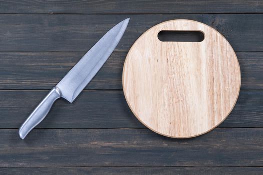 Close up kitchen knife and wooden round empty cutting board on a wooden table