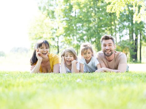 Portrait of happy family lying down in grass in summer park