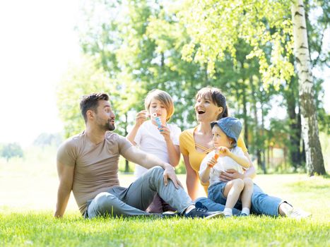 Happy family of mother, father and two children blowing bubbles in summer park