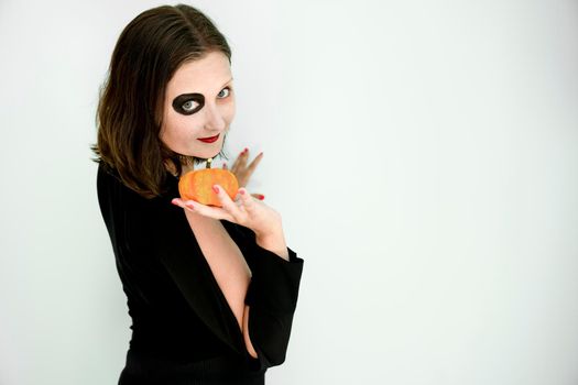 Woman with Halloween makeup on face and pumpkin in hands. Copy space.