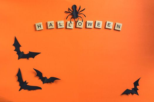 Halloween concept and paper decorations. The inscription from wooden cubes and bats cut from black paper on an orange background. Paper cut style. Top View Copy Space