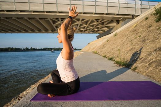 Young woman is exercising outdoor. She is practicing yoga on sunny day. Padmasana, Lotus pose.