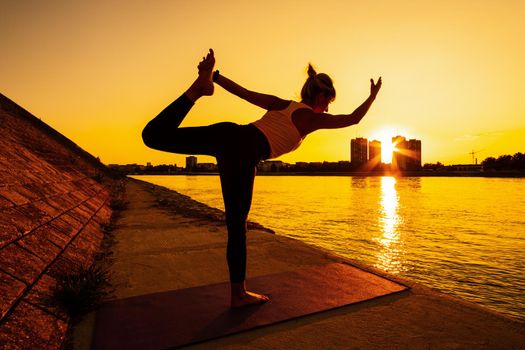 Young woman is exercising outdoor. She is practicing yoga on sunny day. Natarajasana, Shiva posture pose.