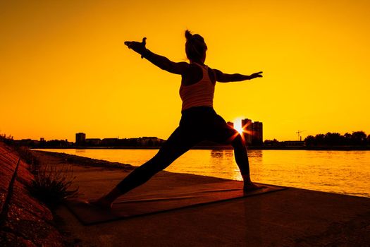 Young woman is exercising outdoor. She is practicing yoga on sunny day. Virabhadrasana / Warrior 2 pose.