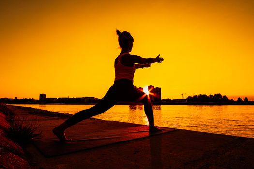 Young woman is exercising outdoor. She is practicing yoga on sunny day. Virabhadrasana / Variation of Warrior pose.