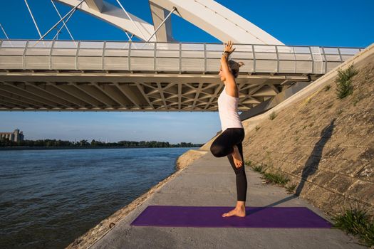 Young woman is exercising outdoor. She is practicing yoga on sunny day. Vriksasana, Tree pose.