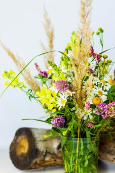 a dry stump, tree bark and a bouquet of wild flowers in a small glass vase. Stylish appearance, layout, personality. Banner, a place for the text. Background for advertising and presentation.