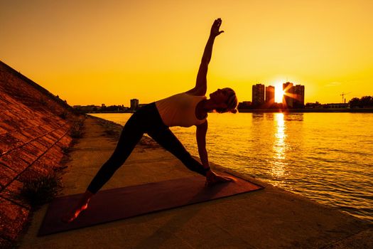 Young woman is exercising outdoor. She is practicing yoga on sunny day. Trikonasana, Bikram triangle left.