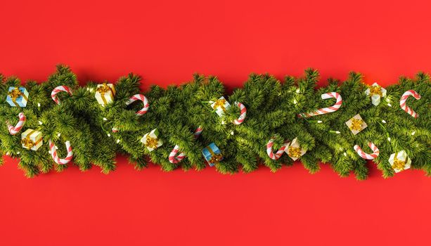 row of Christmas tree garland with gifts and candy ornaments on a deep red background. 3D rendering