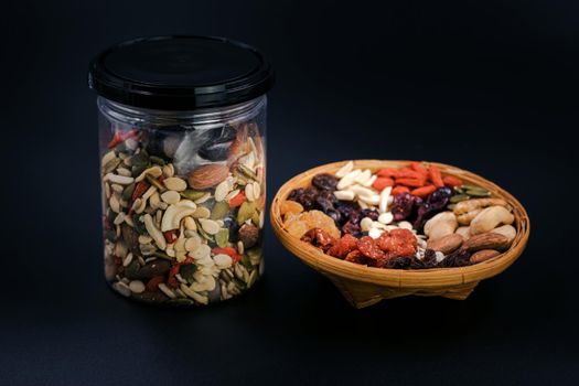 Whole grains and dried fruit in a bamboo plate and plastic bottle on black background.