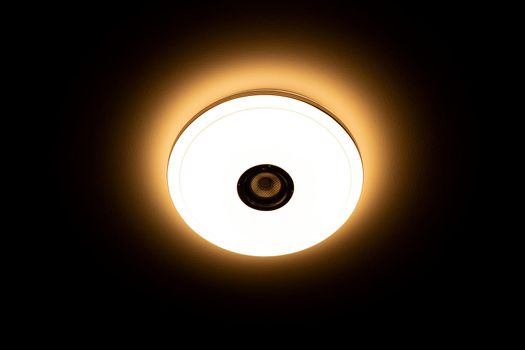 Warm light LED ceiling light with built-in wireless speakers over black background.