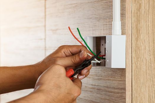 Electrician is stripping electrical wires in a plastic box on a wooden wall to install the electrical outlet.