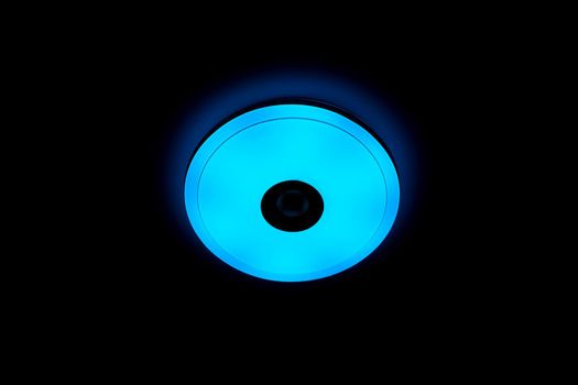 Blue light LED ceiling light with built-in wireless speakers over black background.