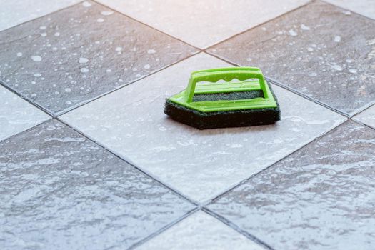 Close up a green plastic brush for scrubbing and cleaning floors placed on a wet tiled floor.