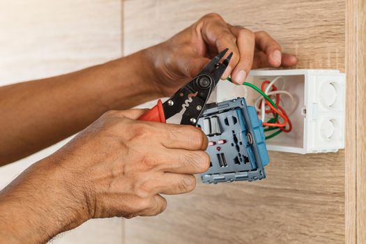 Electrician is stripping electrical wires in a plastic box on a wooden wall to install the electrical outlet.