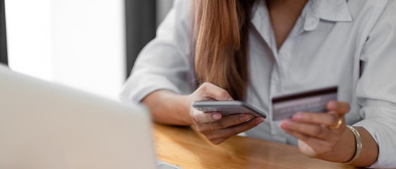 Close up asian woman using smartphone and credit card for online shopping at home with copy space. E-payment technology, shopaholic lifestyle, or mobile phone financial application concept