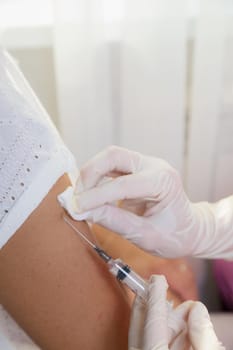 A girl doctor in white gloves makes a vaccination, a vaccine against coronavirus, flu. Coronovirus, disease prevention, Covid-19 of the elderly. Close-up shot in patient's shoulder.