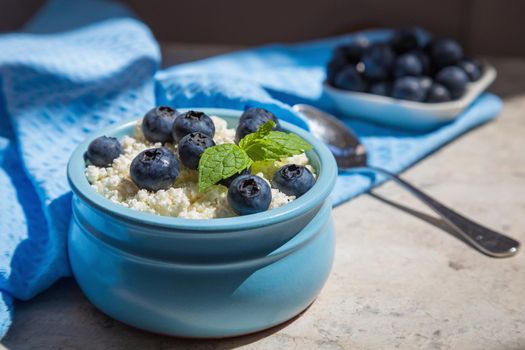 Morning fresh breakfast made from natural products from cottage cheese and blueberries. Nutritious cottage cheese and berries contain healthy vitamins. Blue background.