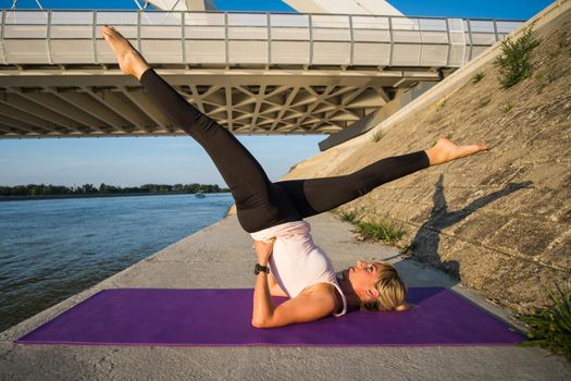 Young woman is exercising outdoor. She is practicing pilates. Scissors exercise.