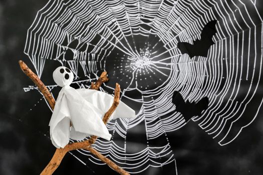 White ghost sits on branch against background of cobwebs and bats. Concept of halloween .