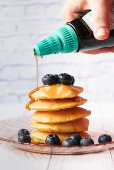 pouring maple syrup on pancakes with fresh berries on plate .