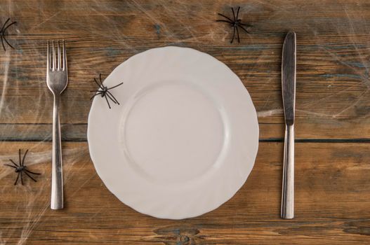 Halloween table setting blank dish, knife and fork with spider web on wood background. Flat lay, top view trendy holiday concept.