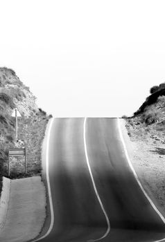 Lonely dizzying road with traffic sign in Spain. Monochrome picture