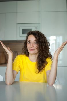 Beautiful curly girl in yellow t-shirt is looking at the camera at home in her apartment, posing with smile, happy people concept.