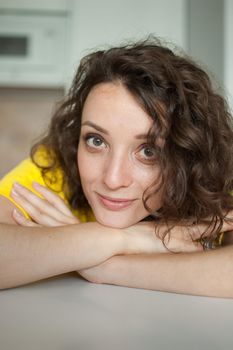 Beautiful curly girl in yellow t-shirt is looking at the camera at home in her apartment, posing with smile, happy people concept.