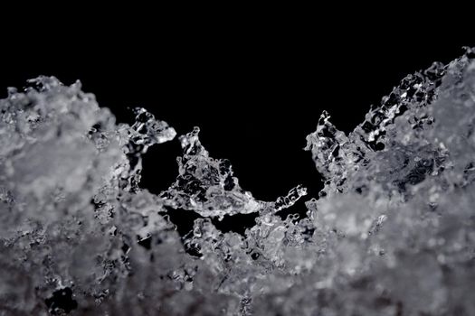 Intricate details of melting water particles. Focus on odd shaped ice crystal in the middle, but plain black background with copy space above.