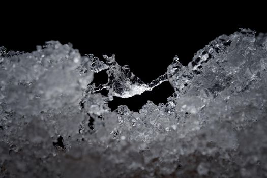 Super close up abstract image of slowly thawing snow. Minute detail of the ice crystals are visible, plain black background. Cold outdoor weather