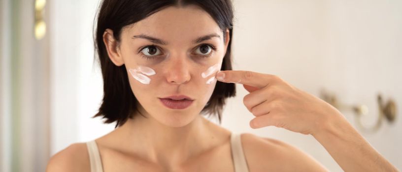 A young pretty girl applies cream stripes on the cheeks, declaring war on dry skin and acne. A woman takes care of the health and hydration of her skin in the bathroom near the mirror.