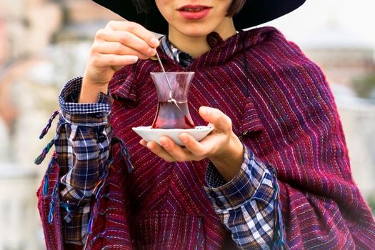 A young girl in a hat and poncho holds traditional Turkish tea in her hands. Istanbul, Turkey