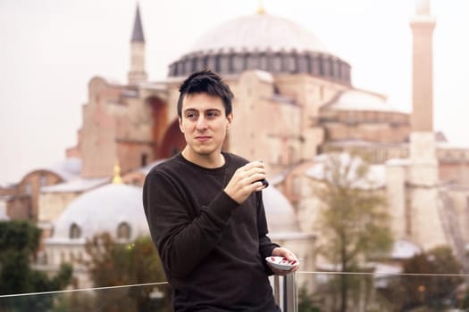 A young man drinks traditional Turkish tea on the background of the Hagia Sophia mosque. Great adventure and tourism in Turkey, Istanbul.