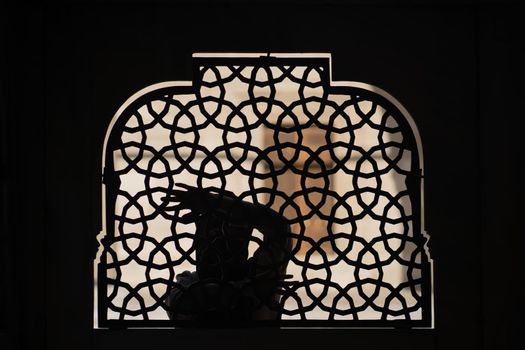 A Muslim girl in a black hijab stands behind a patterned wrought-iron fence. Woman in a conservative Arab country.